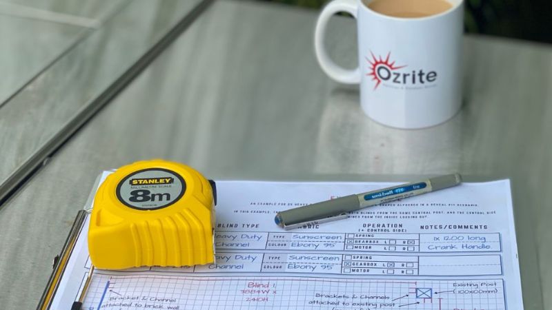 Step 1 of the Ozrite outdoor blinds measuring guide – tape measure, order sheet, and Ozrite mug on a table.