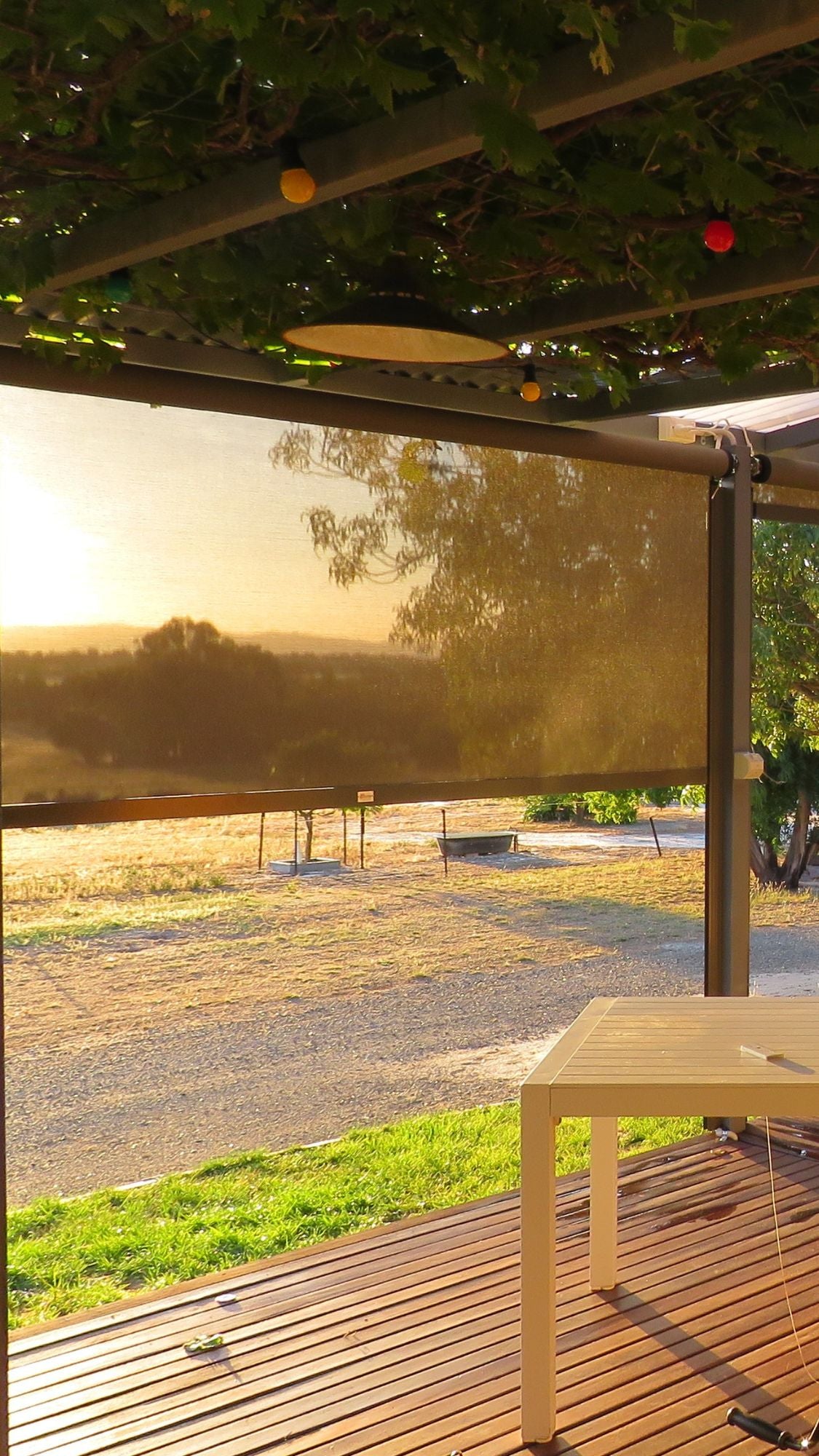 Ozrite outdoor blinds filtering the sunset on a timber deck, providing shade and privacy with a scenic view.